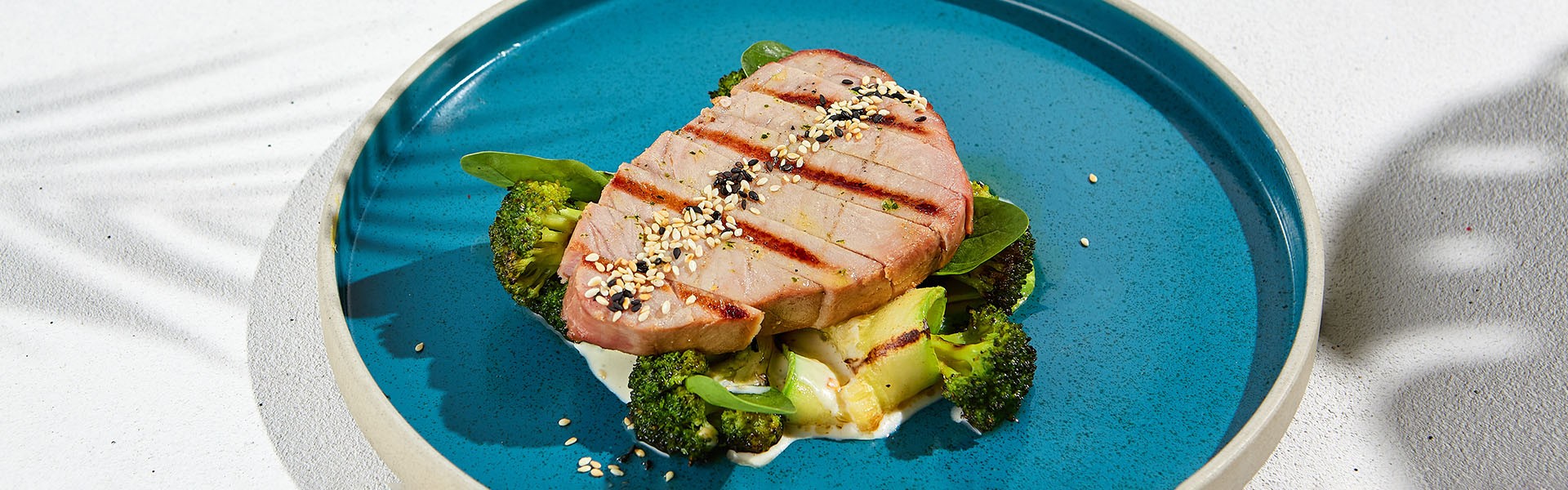 2140967839 Grilled tuna steak with broccoli and zucchini in modern ceramic plate. Healthy food - roasted tuna with green vegetables. Fish dish in minimal style. Tuna fillet in blue plate with hard shadow