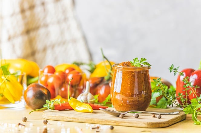 1941990241 Homemade DIY natural canned hot plum sauce chutney with chilli or tkemali in glass jar standing on wooden table with ingredients. Selective focus.