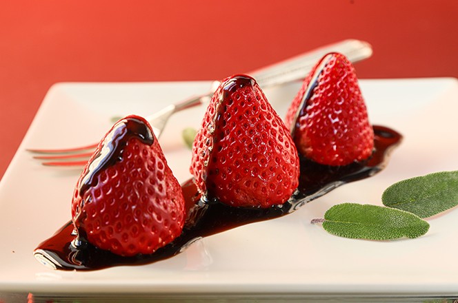 1944071482 Strawberries with balsamic vinegar on a white plate and on a red background. There is a dessert fork in the background. Close up view. Selective focus