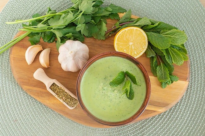 2139971225 Healthy fresh green chutney sauce. With fresh mint pudina and yogurt. Spicy indian cuisine. Served on brown bowl with spices, garlic and parsley on wood board, light background.