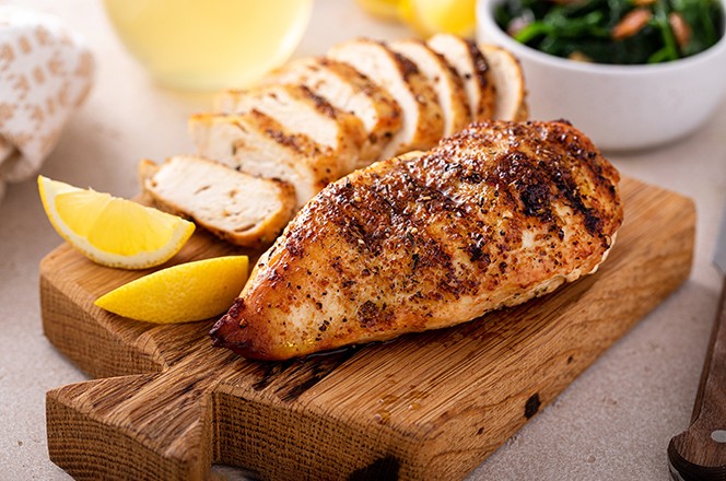 2394668315 Grilled chicken breast whole and sliced on a cutting board with fresh lemon