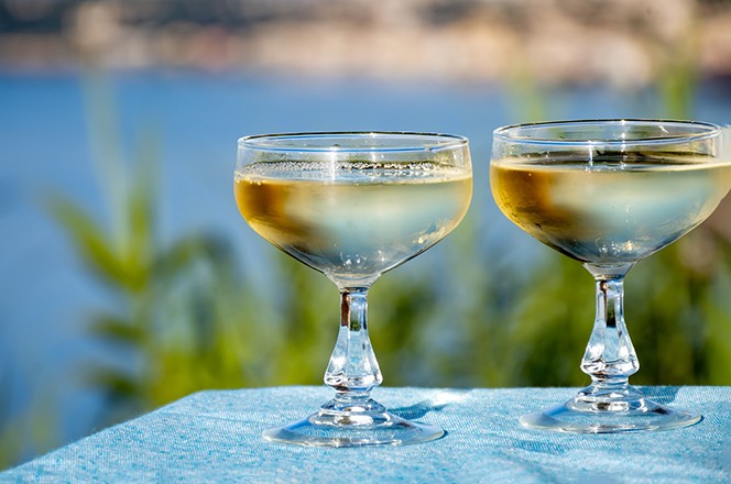 2487572681 Cold sparkling wine, cava or champagne in two coupe glasses on table with sea view near Menton and Monte-Carlo, French Riviera, France is summer