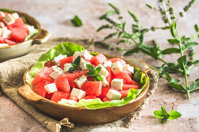 2491257139 Fresh watermelon salad with feta cheese and mint on beige textured background, decorated with a sprig of mint