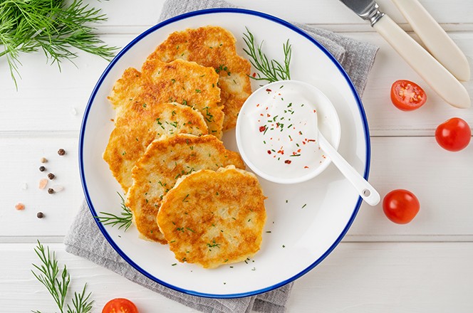 2311688833 Palacinke od krumpira, latkes ili draniki sa svje im zacinskim biljem i kiselim vrhnjem na tanjuru na bijeloj drvenoj pozadini.