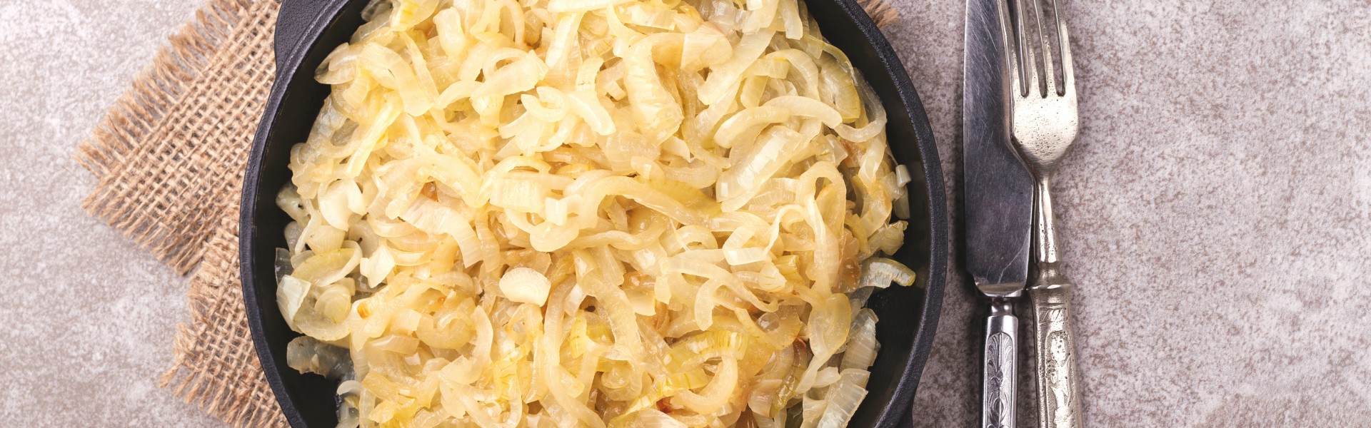 Homemade caramelized onions in frying pan. Hot vegetarian food.