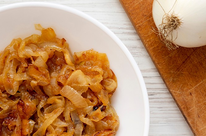 Homemade caramelized onions on a white plate on a white wooden table, top view. Flat lay, overhead, from above. Closeup.