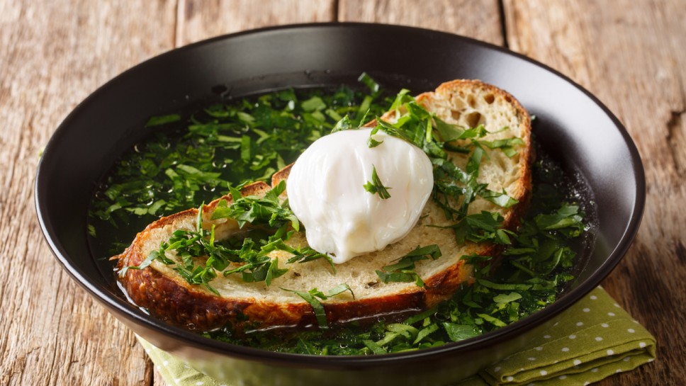 Summer Acorda Soup with cilantro, garlic, homemade bread and poached egg close-up in a bowl on the table. horizontal
