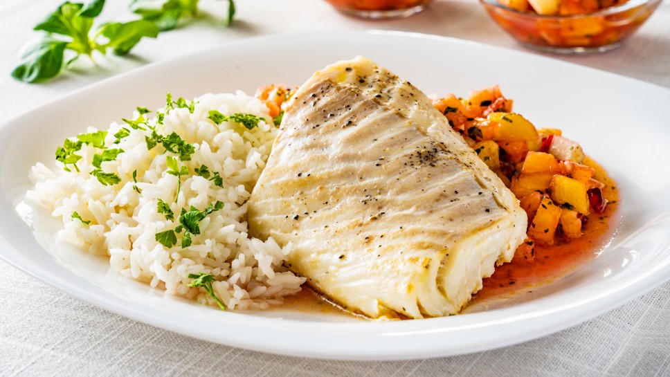 Fish dish - fried cod fillet with boiled white rice and fresh fruit salsa on white table 