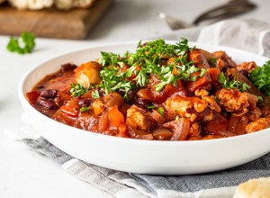 Meat stew with red beans, bell pepper and onion in tomato sauce in a white plate over light grey slate or stone background. 