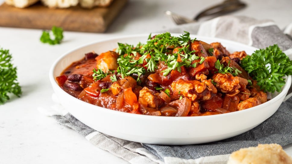 Meat stew with red beans, bell pepper and onion in tomato sauce in a white plate over light grey slate or stone background. 