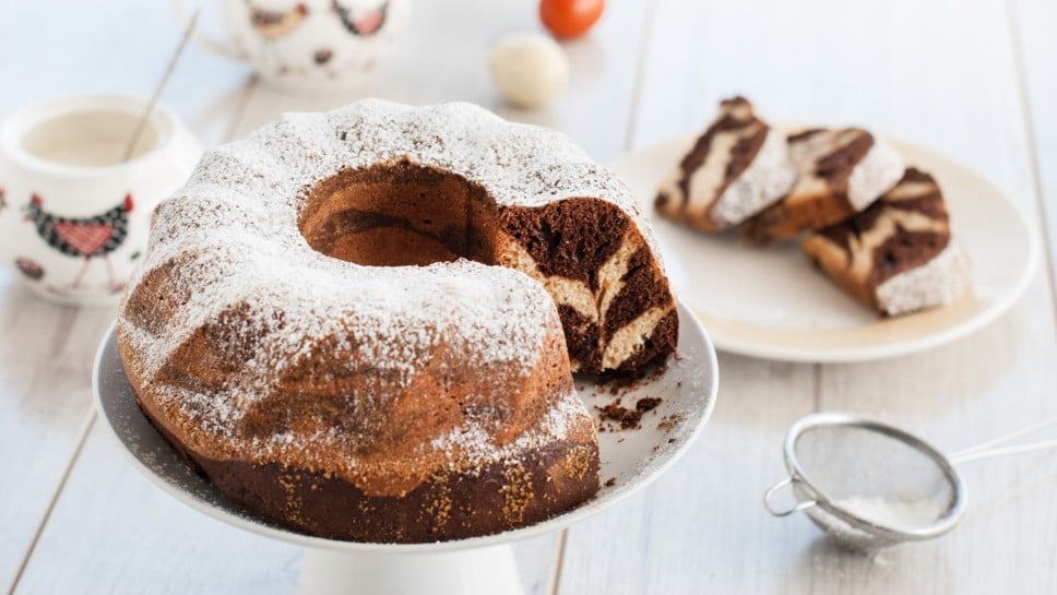 Marble bundt cake with power sugar and easter eggs on wooden table. Bundt cake easter. Food and drink.