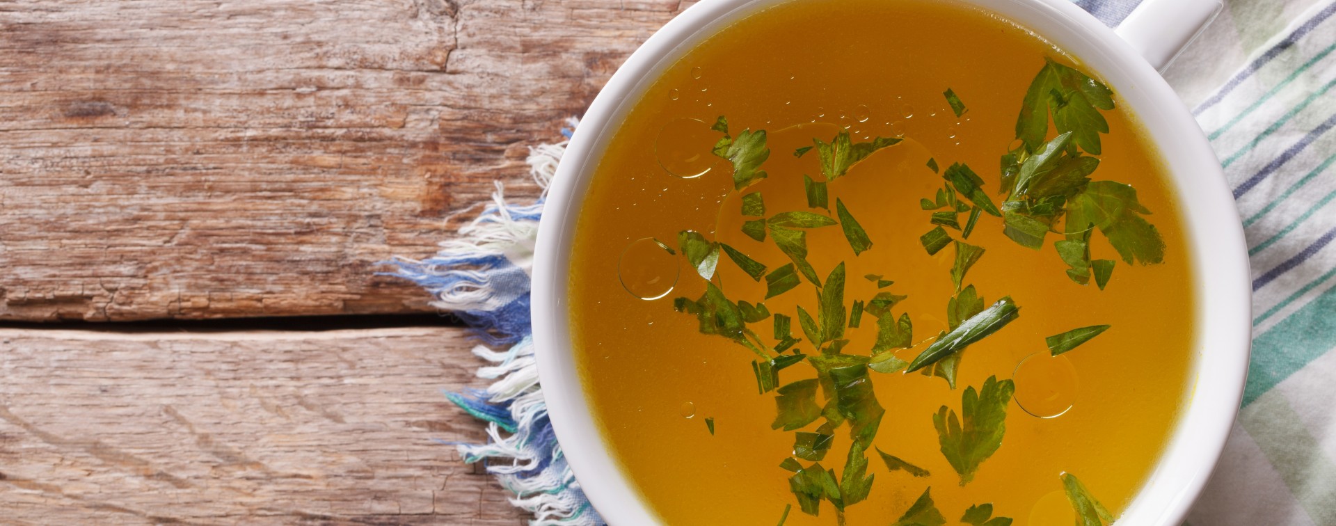 Tasty meat broth with parsley in a white bowl closeup. horizontal view from above
