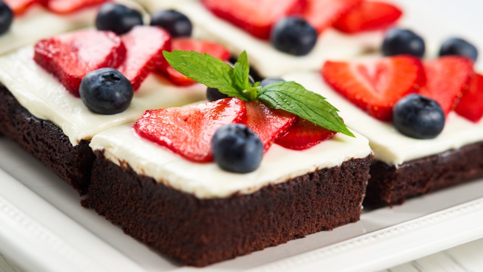 Pieces of chocolate cake with icing, strawberry, blueberry and mint on a plate