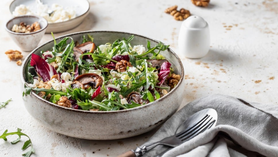Healthy diet salad with feta cheese, arugula, mushrooms, walnut in ceramic bowl on textured background with text space. Fresh summer lunch or dinner. Horisontal