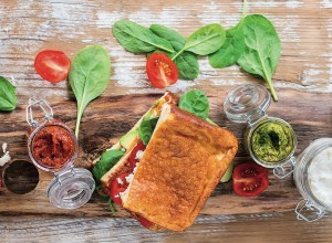 Low-carb gluten free Cloud bread veggie sandwich with spinach, avocado, feta cheese, tomatoes and pesto sauce, served on cutting board with jars of ingredients over wooden background. Top view