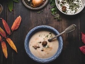 Vegetarian chestnuts creamy soup bowl on dark rustic kitchen table background with cooking pot ,ingredients and autumn leaves , top view. Healthy seasonal winter or autumn food and eating