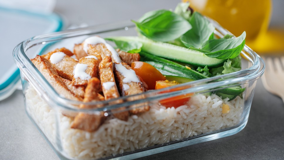 Lunch to go chicken, cucumber and rice in glass lunchboxes on grey table. Closeup