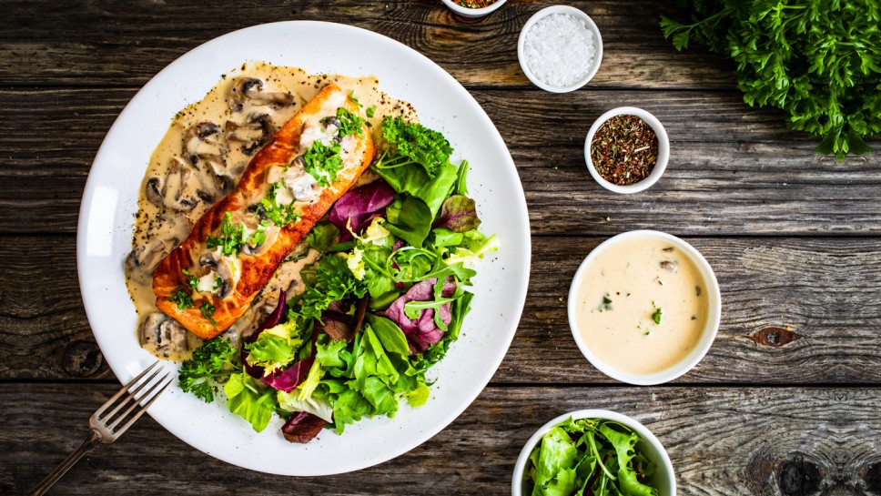 Fried salmon steak in mushroom sauce and vegetable salad served on wooden table