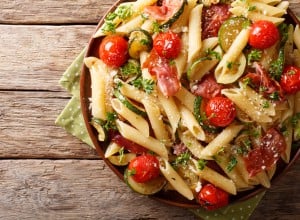 Italian penne pasta with ham prosciutto, tomato, zucchini and parmesan close-up on a plate.  horizontal view from above