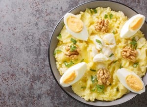 Atascaburras a Delicious Salt Cod and Potato dish with slices of hard boiled egg, walnuts and a dash of oil closeup on the bowl on the table. Horizontal top view from above