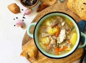 Homemade hot vegetable soup with chicken, mushrooms and bulgur on a white countertop. Top view flat lay background.