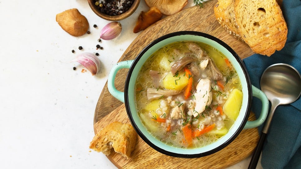 Homemade hot vegetable soup with chicken, mushrooms and bulgur on a white countertop. Top view flat lay background.