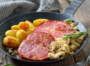 German food - Smoked neck of pork with sauerkraut and fried baby potatoes served in an iron frying pan on an old wooden table