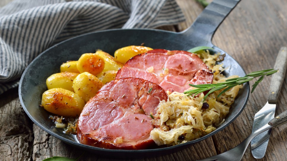German food - Smoked neck of pork with sauerkraut and fried baby potatoes served in an iron frying pan on an old wooden table