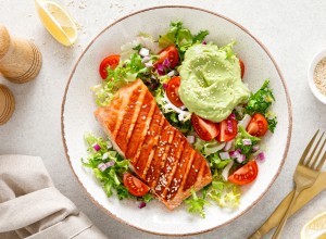 Grilled salmon fish fillet and fresh green lettuce vegetable tomato salad with avocado guacamole. Top view.