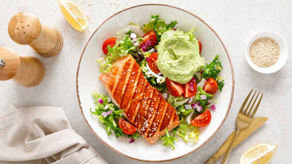 Grilled salmon fish fillet and fresh green lettuce vegetable tomato salad with avocado guacamole. Top view.