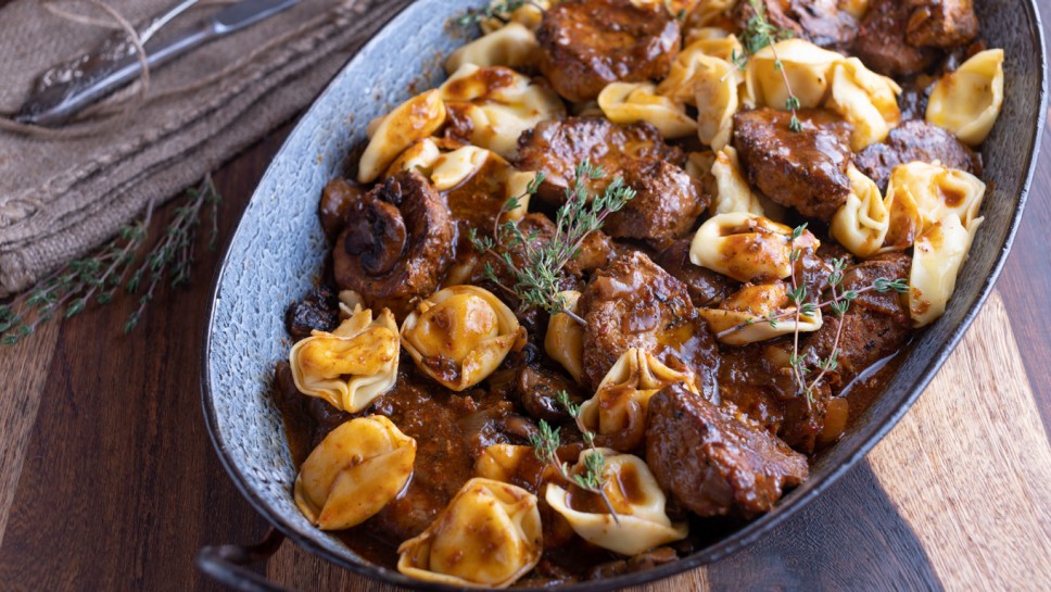 Meat dish with pasta and mushroom sauce. Delicious braised pork tenderloin with tortellini and brown gravy.
