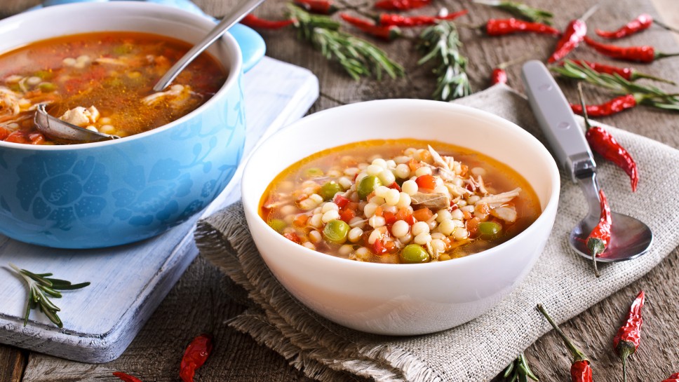 Soup with small pasta, vegetables and pieces of meat in a ceramic bowl on a wooden surface