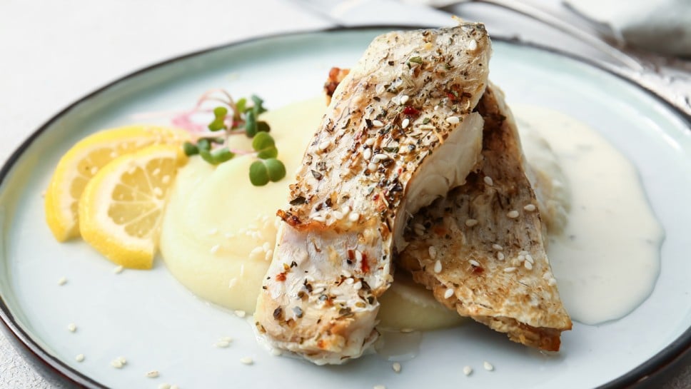 Plate with baked cod fillet, sauce and mashed potatoes on table in restaurant