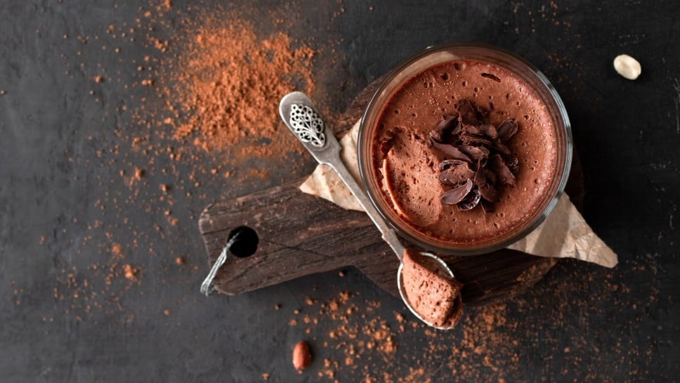Vegan chocolate mousse glass on a wooden board with a spoon on a dark background. Top view. Flat lay