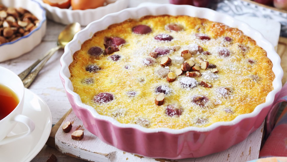 French cuisine. Red grape clafoutis, almondes dressing and cup of tea on light background