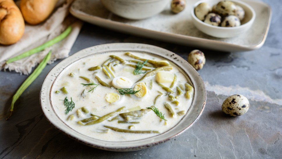 Dairy green bean soup with potatoes and dill in a ceramic bowl served with baguette