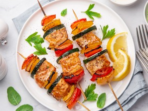 Grilled salmon and vegetables skewers on white plate, top view