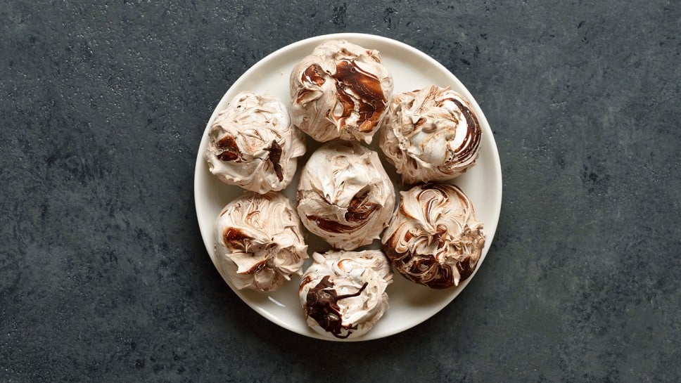 Chocolate meringue cookies on plate over dark stone background. Top view, flat lay