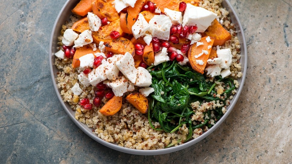 Quinoa with feta, roasted sweet potato, pomegranate and wilted spinach, horizontal shot on a grey and beige granite background, elevated view