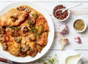rustic style of Chicken Marsala, Italian-American dish of golden pan-fried chicken breasts and mushrooms in a rich Marsala wine sauce on a white platter on a wooden table, flatlay