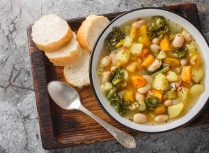 Autumn vegetarian Frantoiana soup with beans, potatoes, pumpkin, kale, carrots, onions and celery close-up in a bowl on the table. Horizontal top view from above