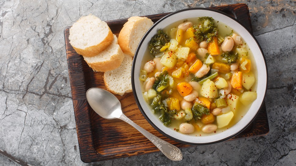 Autumn vegetarian Frantoiana soup with beans, potatoes, pumpkin, kale, carrots, onions and celery close-up in a bowl on the table. Horizontal top view from above