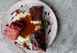 Close-up of delicious ribs in different sauces served with mashes potato covered with beer and horseradish sauce and cherry tomatoes. Copyspace.