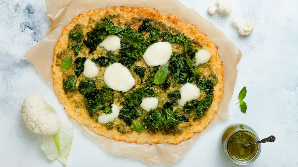 Cauliflower pizza crust with pesto, kale, mozzarella cheese and greens