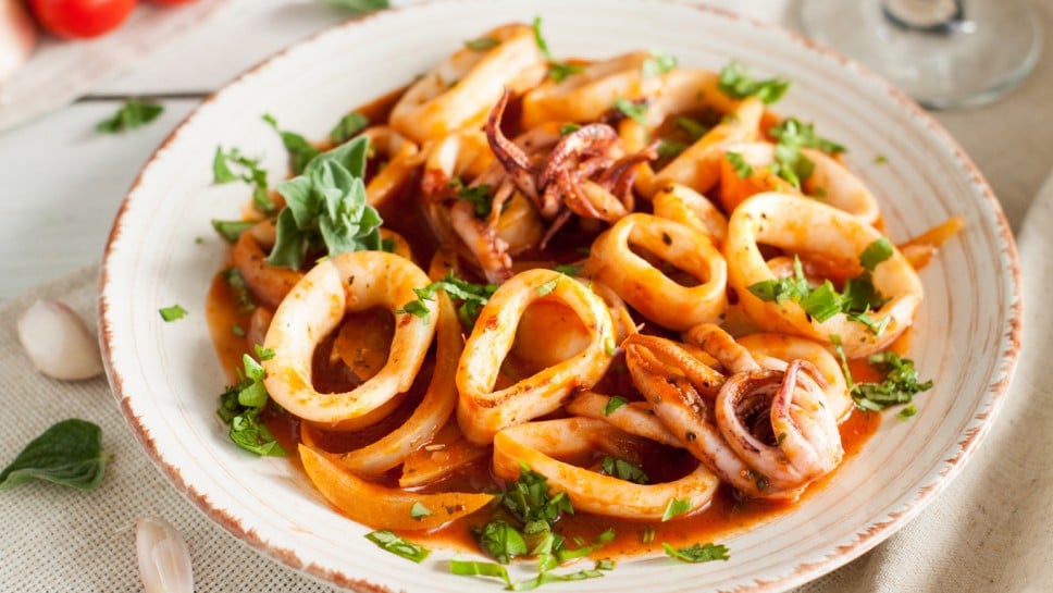Salad with calamari, octopus, parsley and tomato sauce on light wooden table