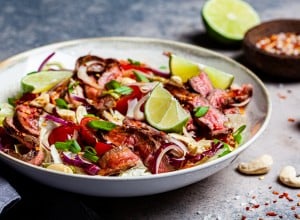 Asian beef salad with vegetables and nuts in a white bowl on a dark background. Asian food concept.