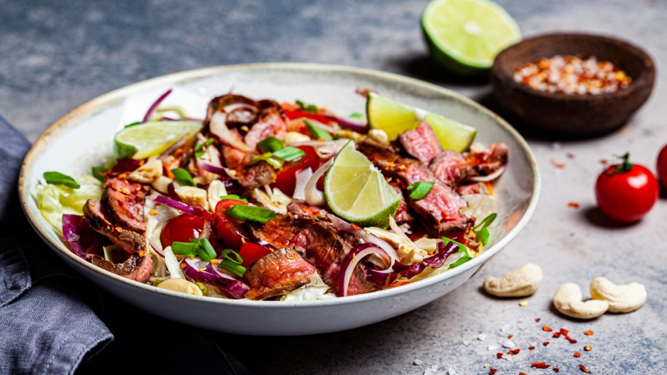 Asian beef salad with vegetables and nuts in a white bowl on a dark background. Asian food concept.