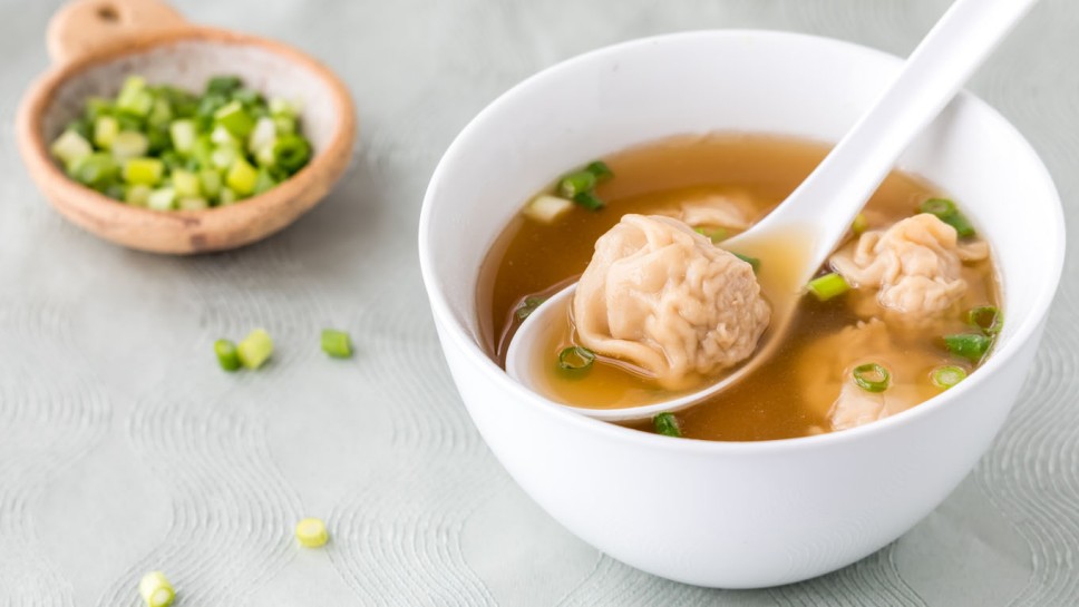 A bowl of hot wonton soup with slices of green onion.