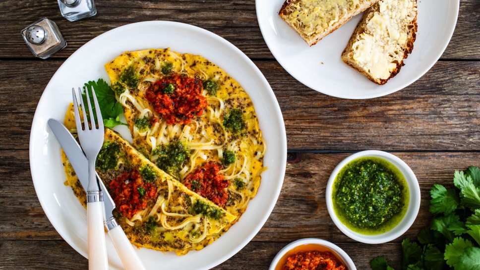 Tagliatelle omelet - scrambled eggs with mozzarella cheese, tagliatelle, basil and tomato pesto on wooden table 