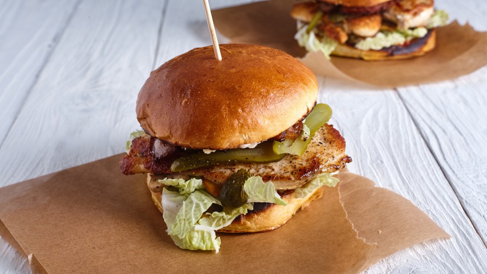 Two burgers with chicken breast, cheese sauce and mushrooms on wood background
